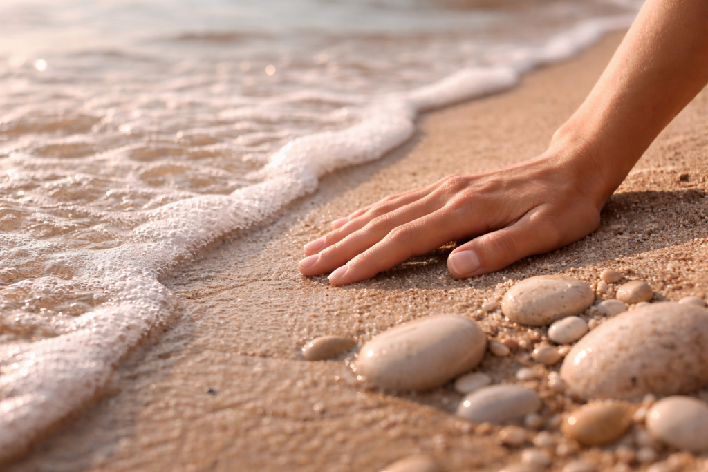 Main posée sur le sable avec galets et écume de vague - Thérapie individuelle femmes hommes LGBT+ Nathalie Flamme sexothérapeute Lunel